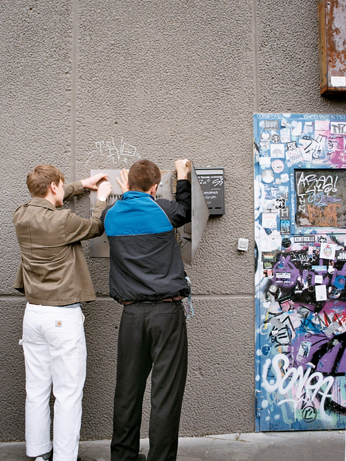 Two people attach the letterbox to a house wall.
