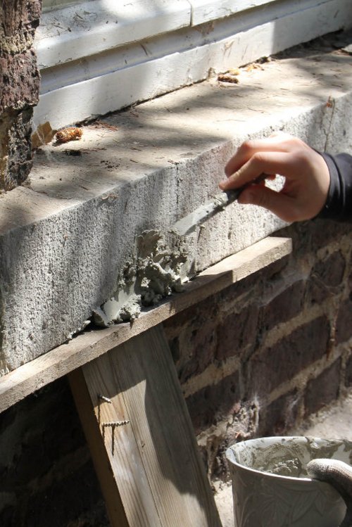 A person repairs a window sill with liquid concrete.